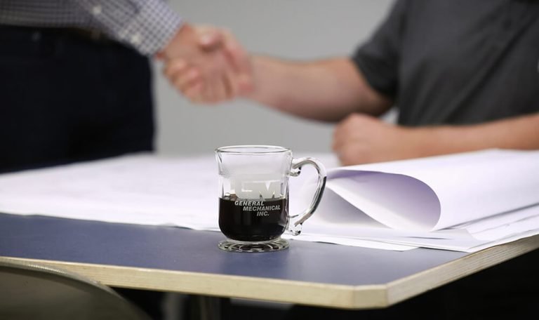 Building Trusted Partnerships Handshake over project documents on a table, representing a professional agreement with General Mechanical